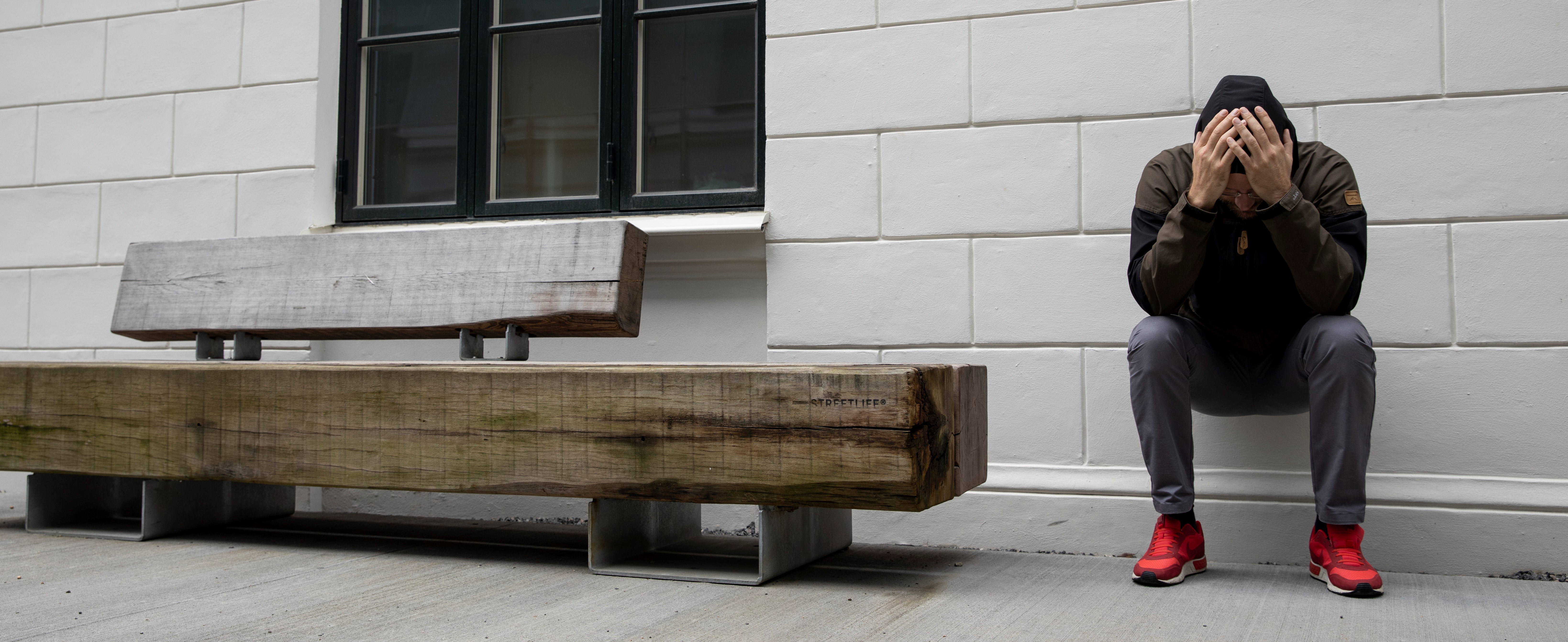 Man sitter lutad mot en vägg och håller händerna för ansiktet. 