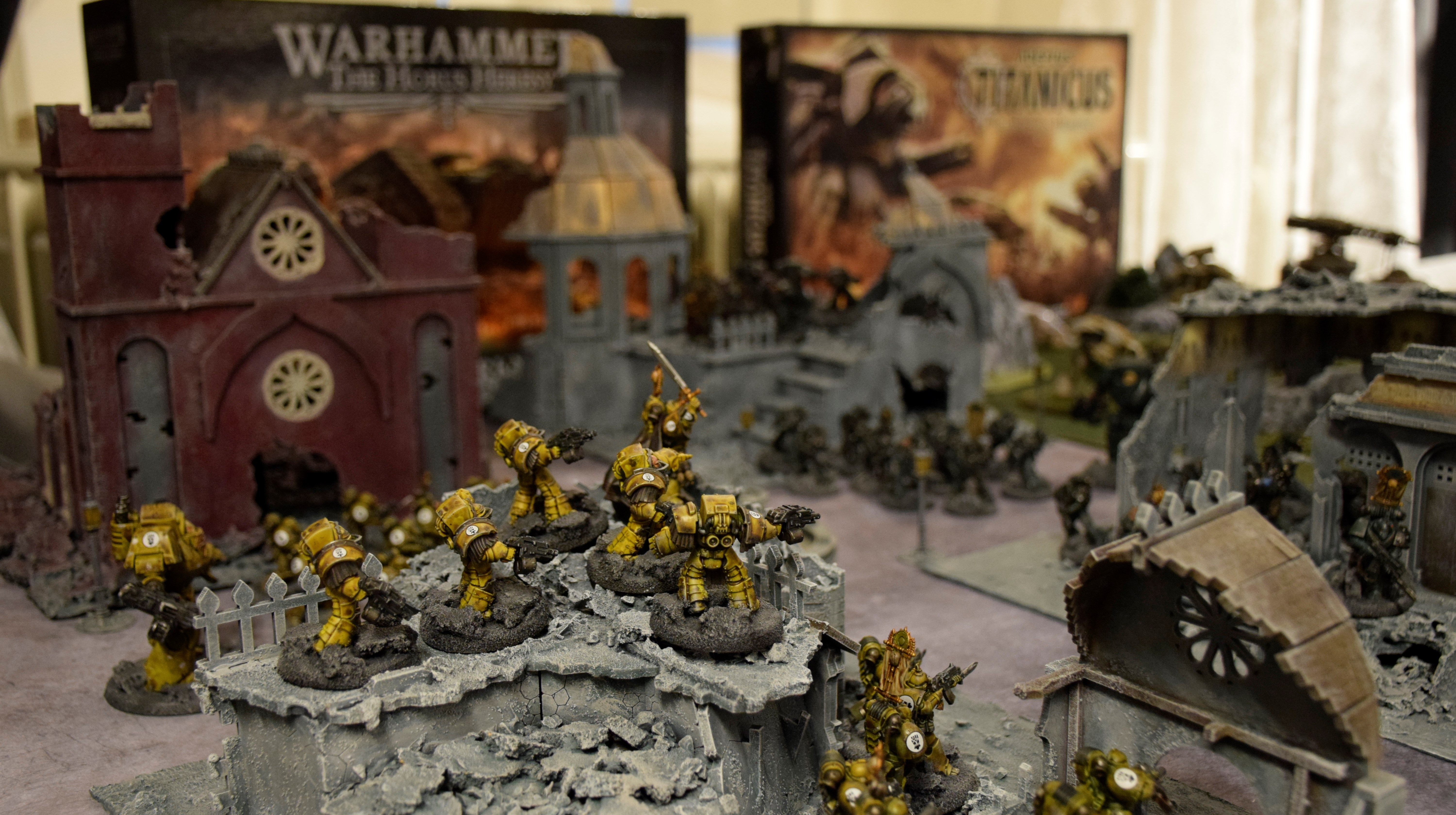 Ett bord med byggnader som tillhör ett spel. Små spelfigurer i plast drabbar samman i förgrunden. 