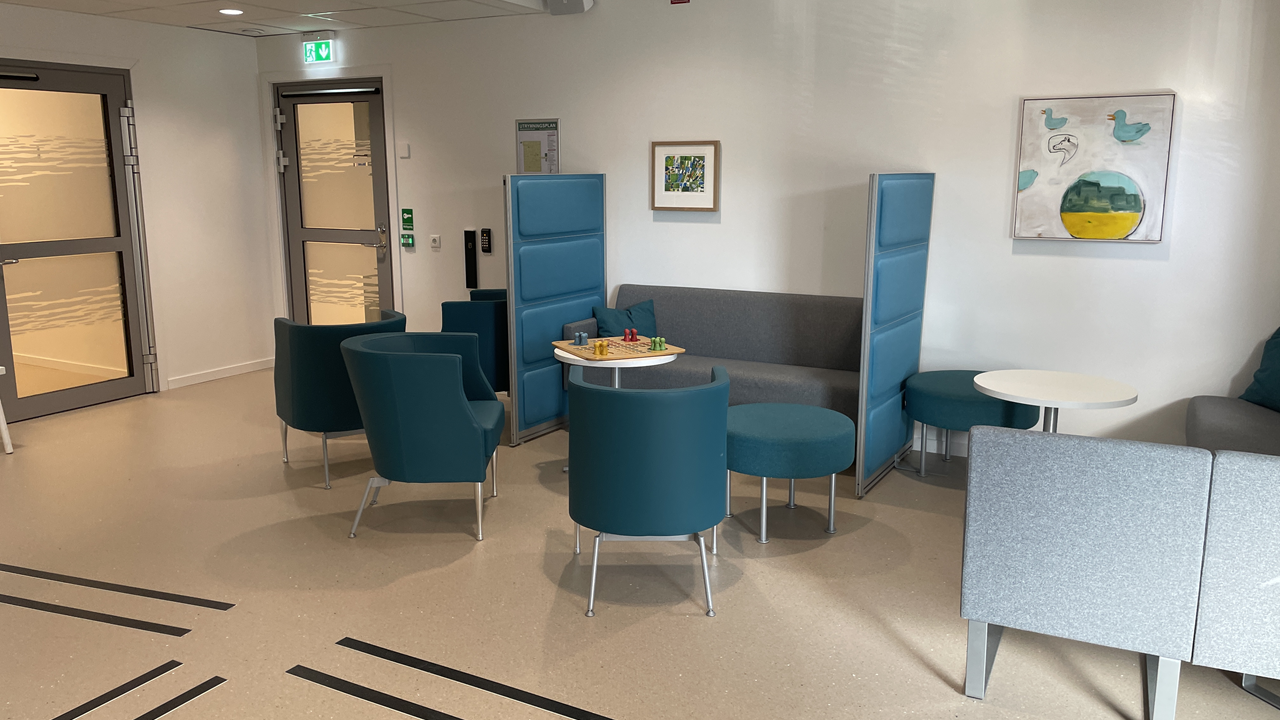 Väntrum med blåa och gråa fåtöljer, samt små vita bord.