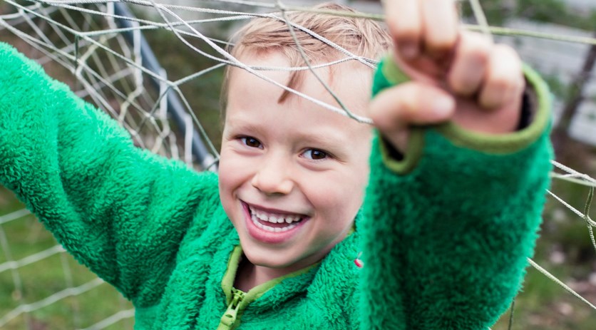 Ett barn som står och håller i nätet i ett fotbollsmål.