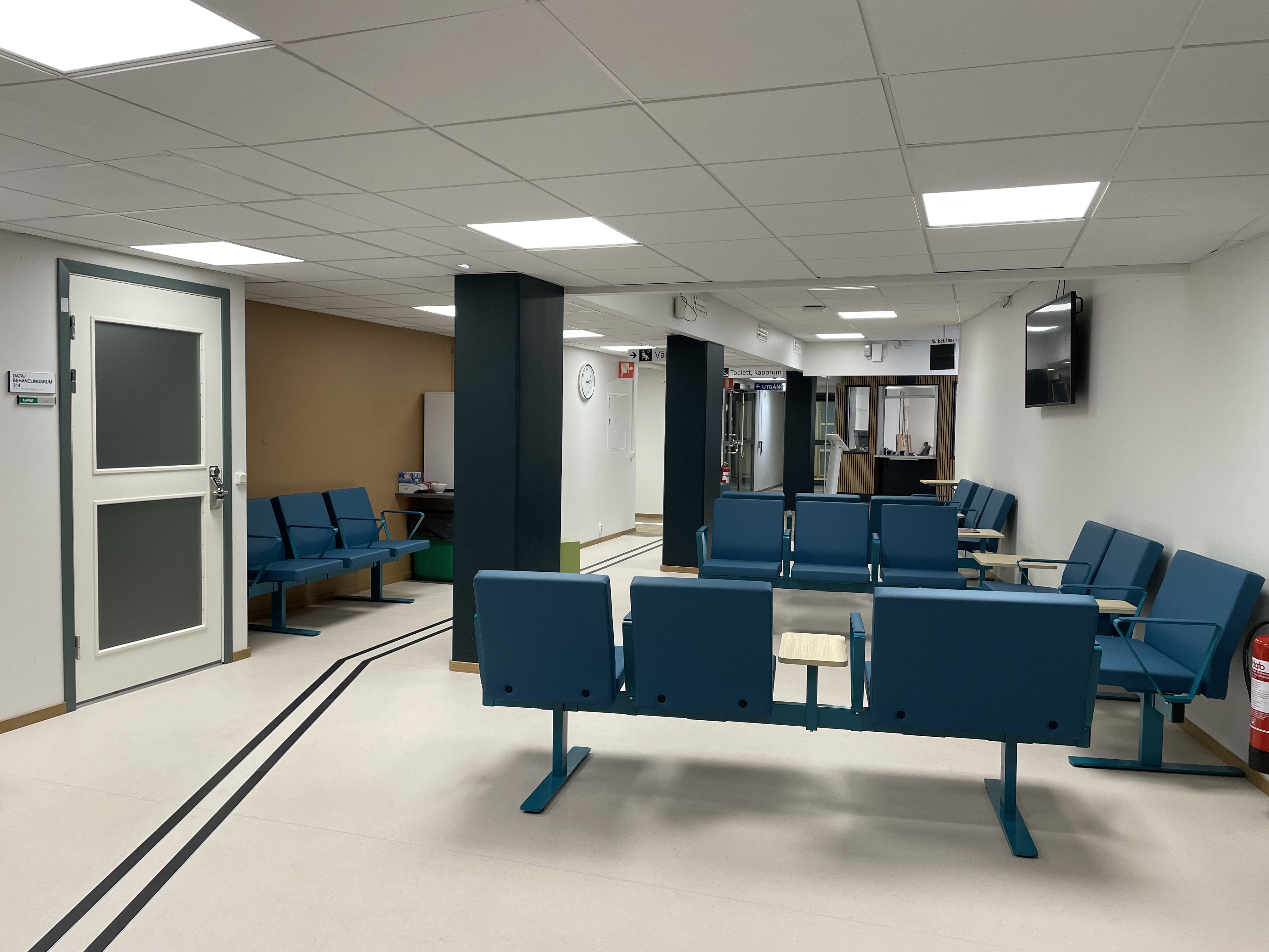 Väntrummet med blå sittmöbler och vitt golv med ledstråk.