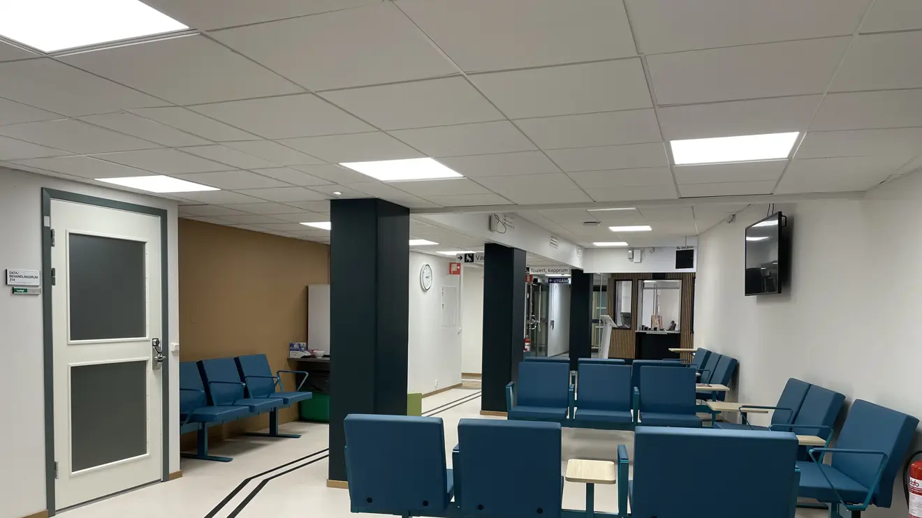 Väntrummet med blå sittmöbler och vitt golv med ledstråk.