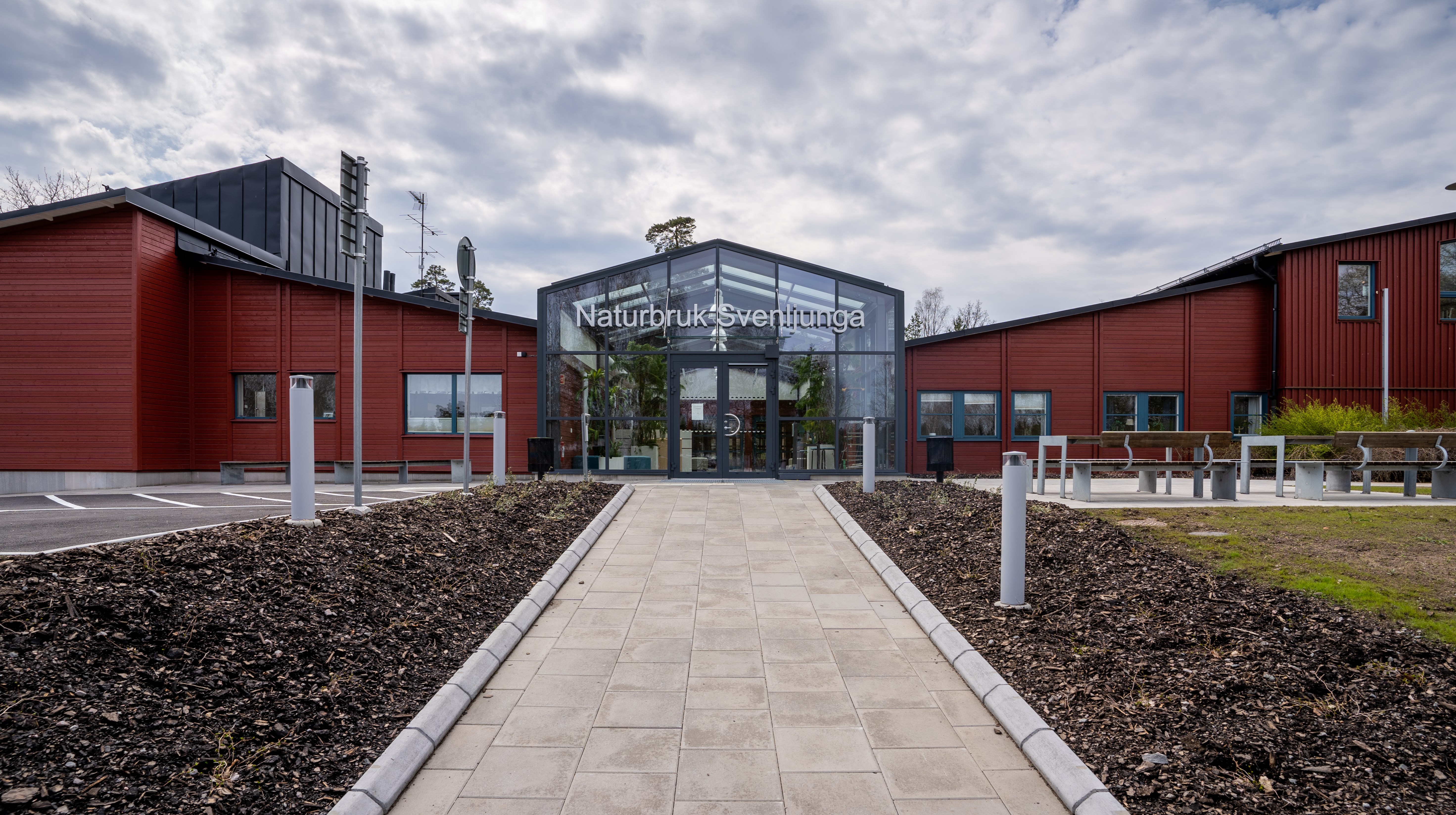 En stengång leder fram till röd huvudbyggnad med glasentré