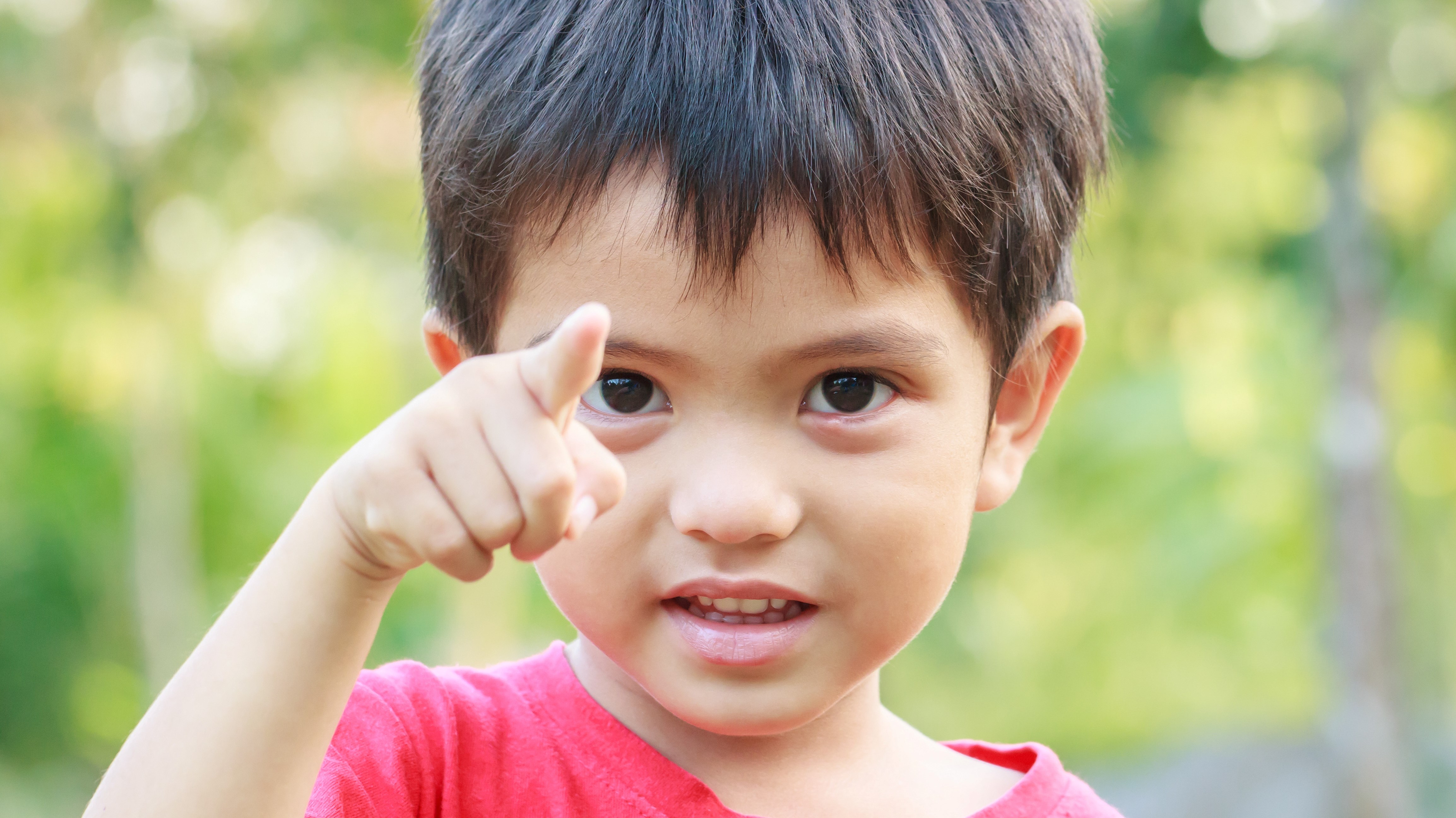 En pojke i femårsåldern tittar in i kameran och pekar mot oss.