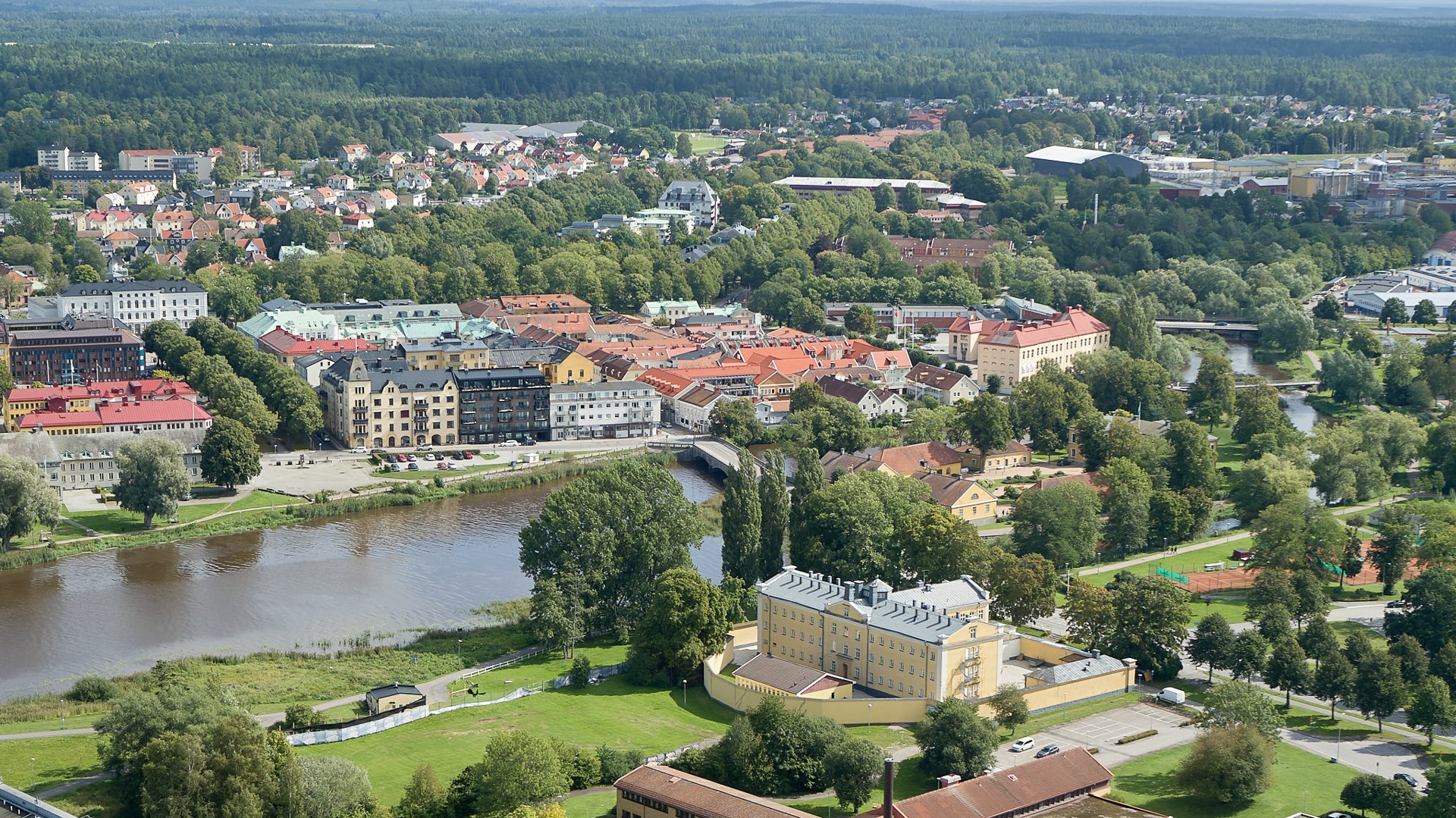 Drönarbild över tätort med vattendrag, med skog i bakgrunden