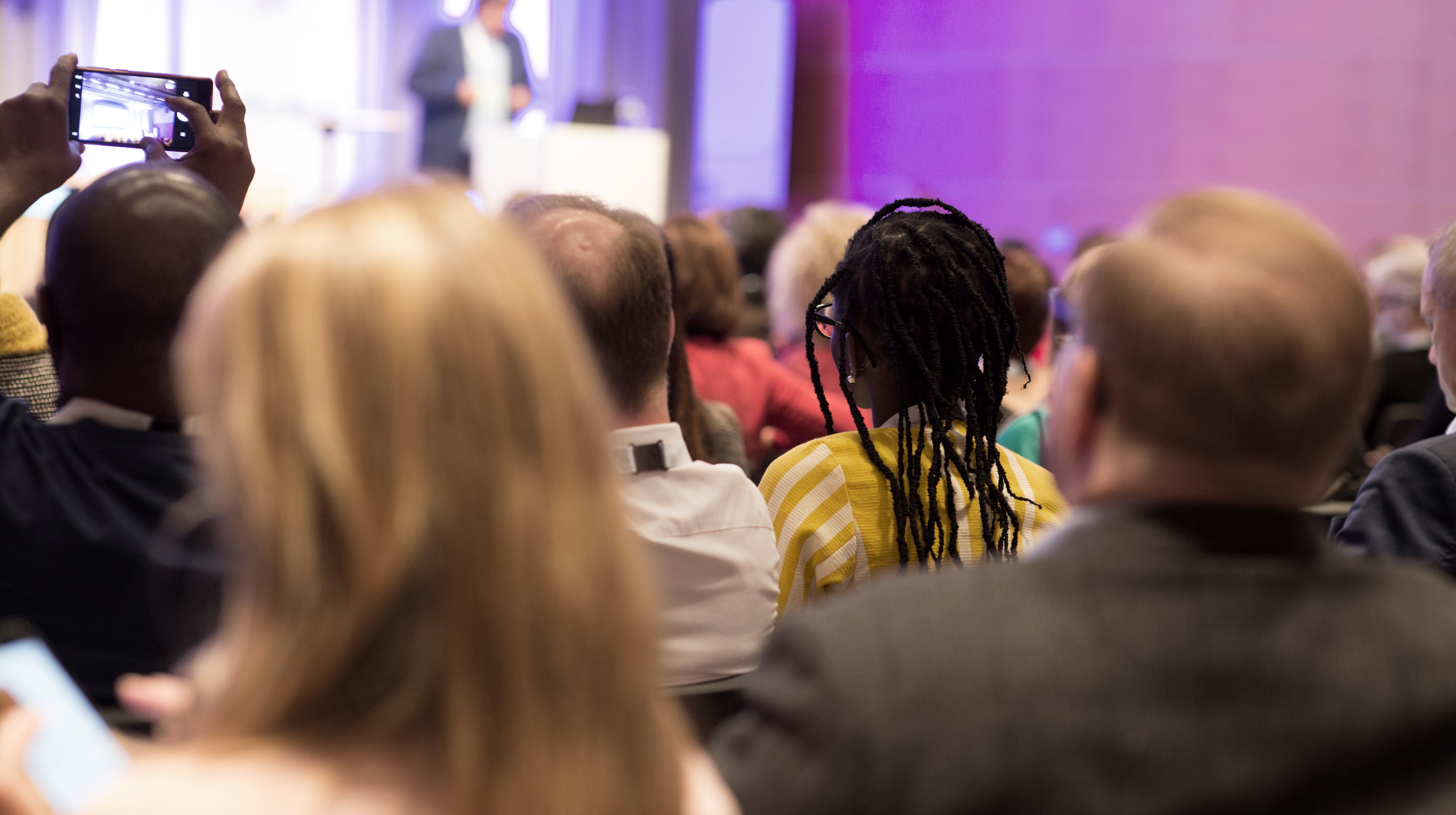 Bild på publik som lyssnar till en talare.