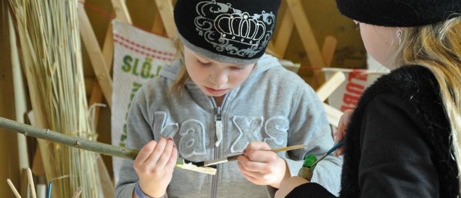 Två barn målar på täljda pinnar