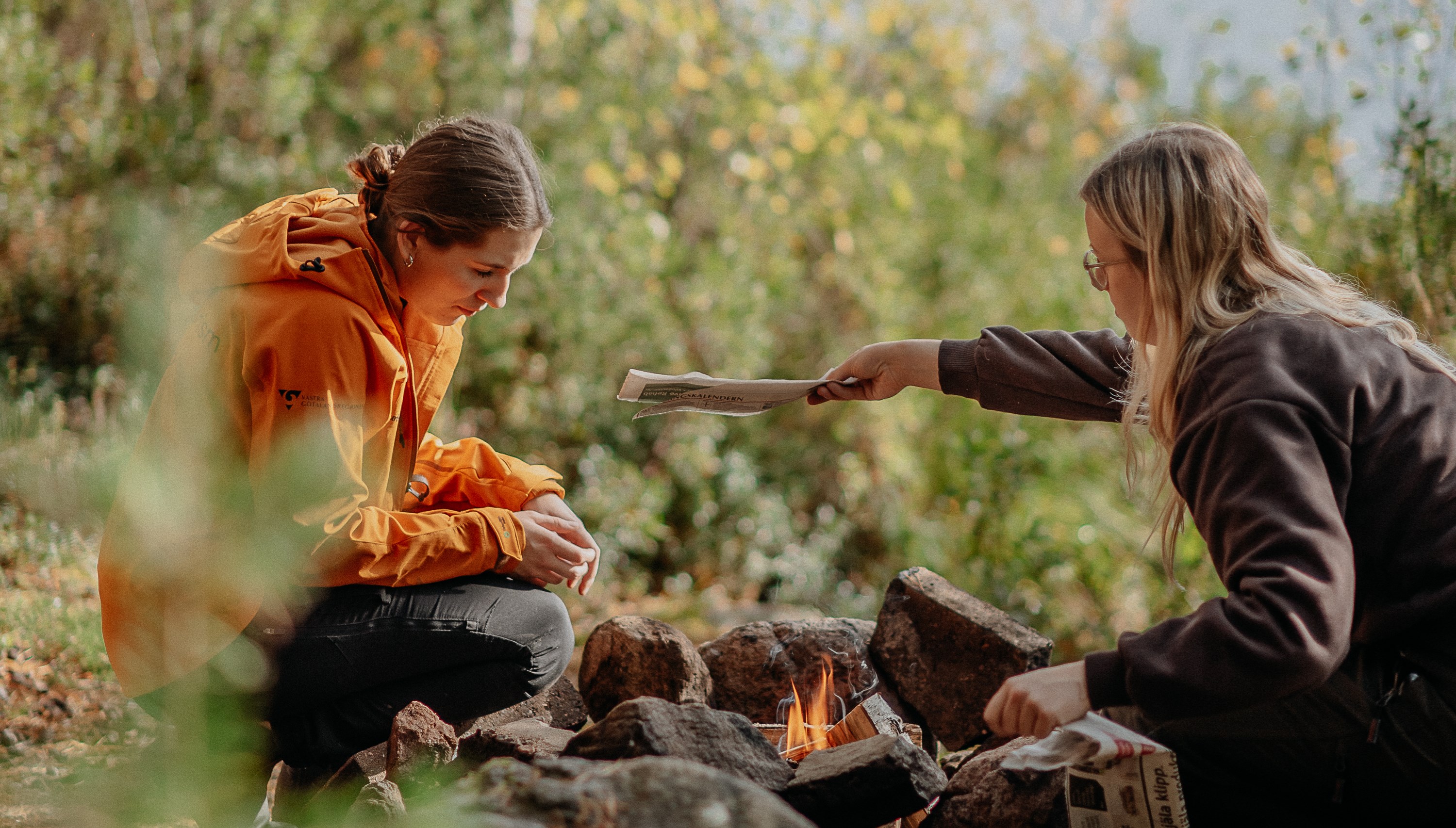 Två elever sitter framför en öppen eld i skogen