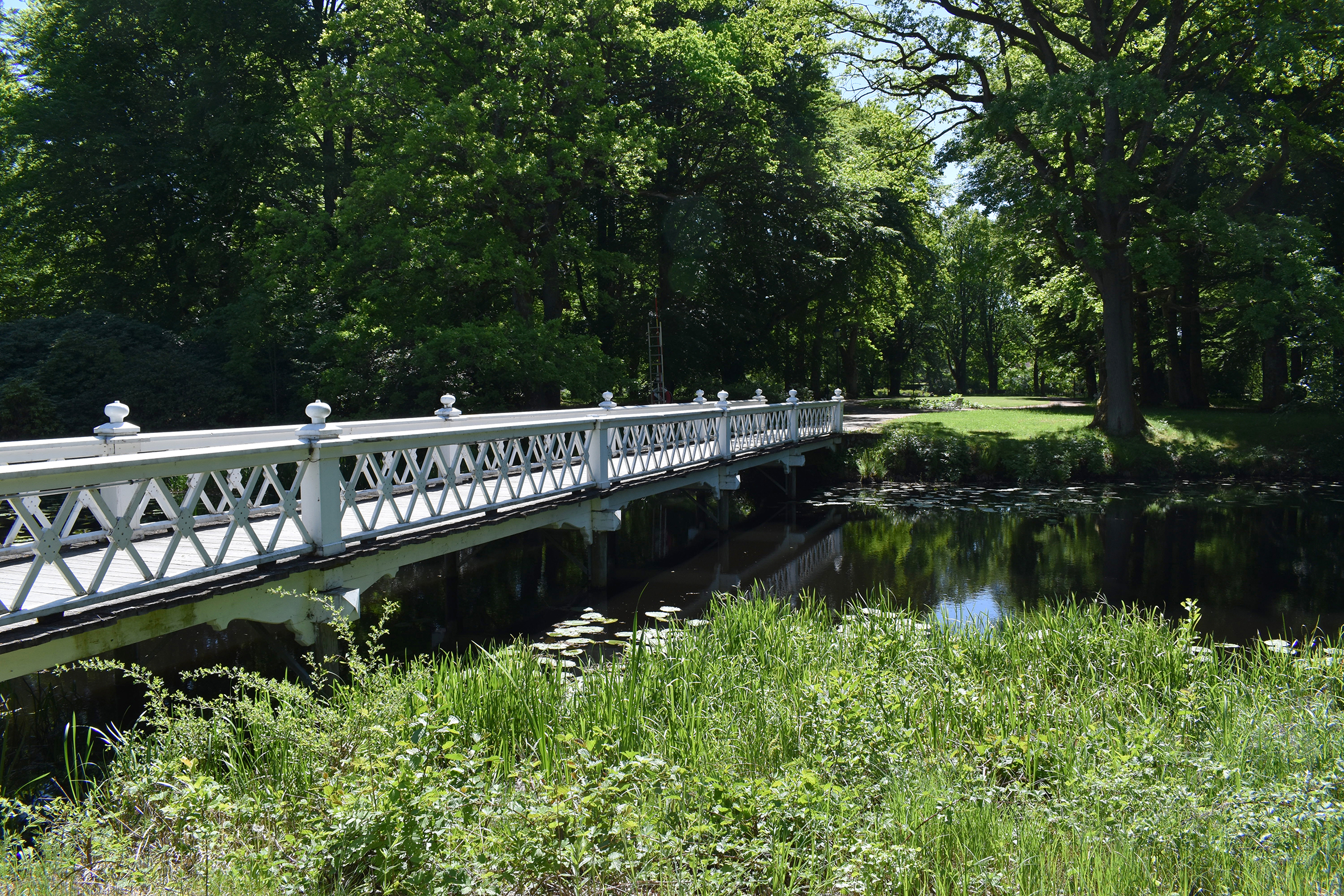 En vit bro som går över en å i Nolhagaparken.