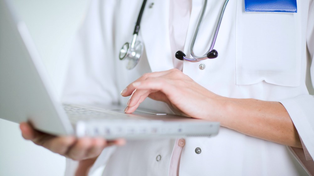 Läkare i ljusa kläder som står med dator och läser av information.
