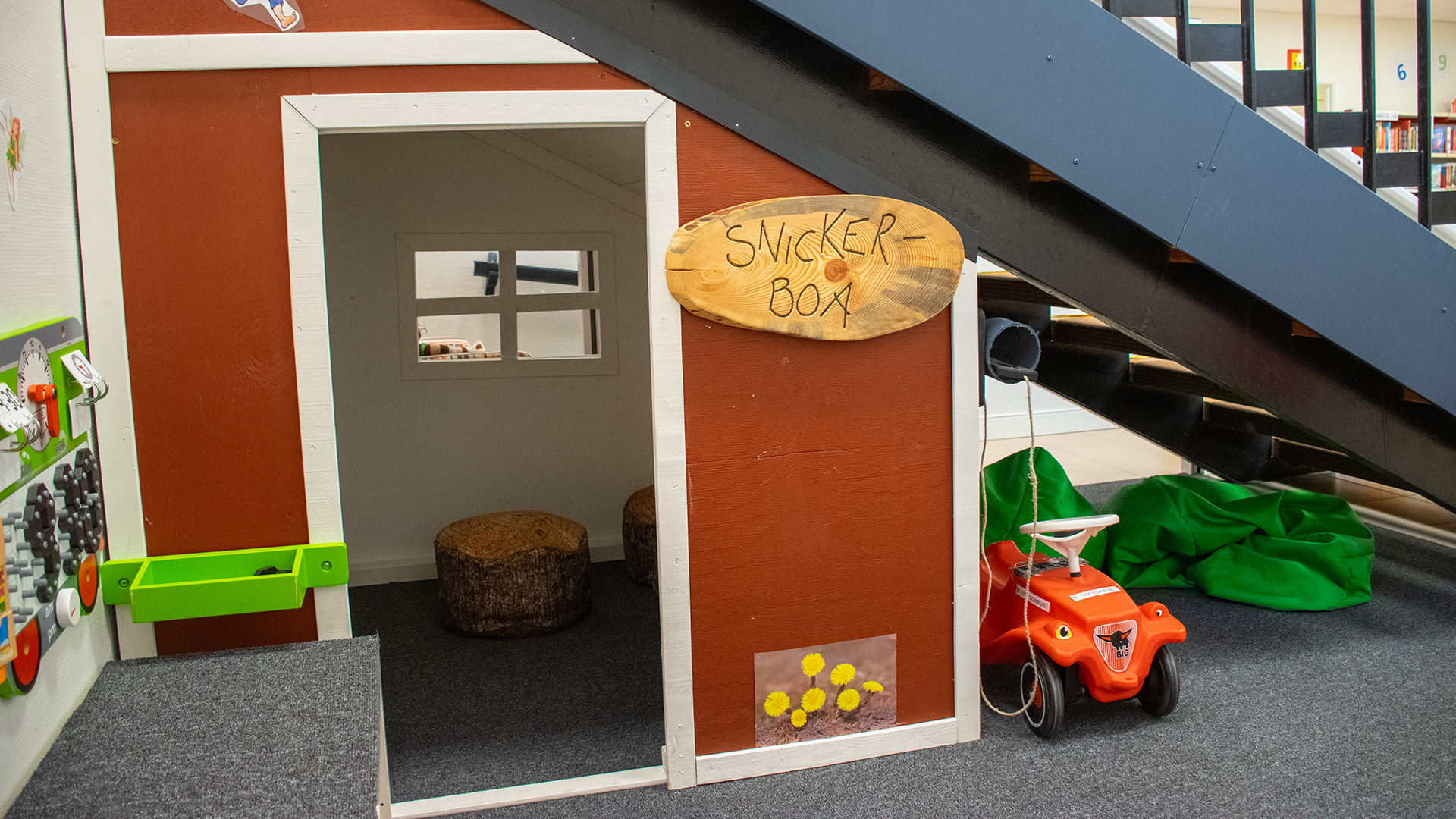 Under trappan finns snickerboa, ett litet krypin, rött med vita knutar. Några kuddar i form av stubbar finns inne i boden. Utanför står bland annat en röd bobbycar. 