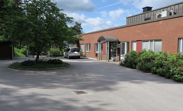 Låg röd tegelbyggnad med rund vändplats med träd i mitten framför.