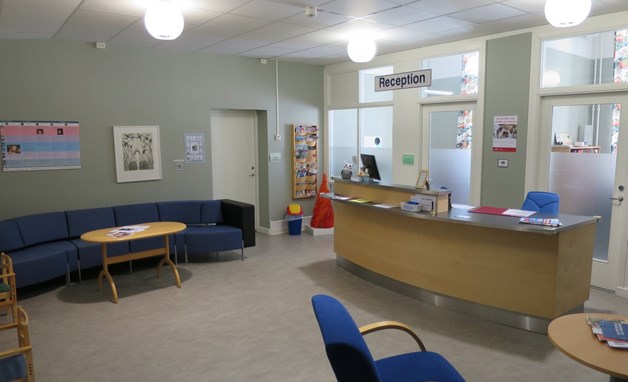 Väntrum med receptionsdisk som är lite svängd och soffa. 